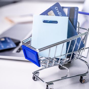 Office online paying, stay home shopping, electronic payment with credit card concept, laptop on white table background with shop cart, close up.