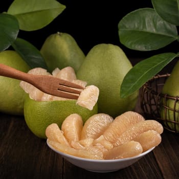 Fresh pomelo, pummelo, grapefruit, shaddock on wooden table over black background, close up, copy space. Fruit for Mid-autumn festival.