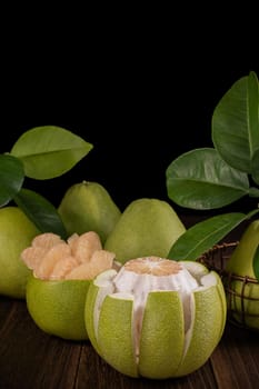 Fresh pomelo, pummelo, grapefruit, shaddock on wooden table over black background, close up, copy space. Fruit for Mid-autumn festival.