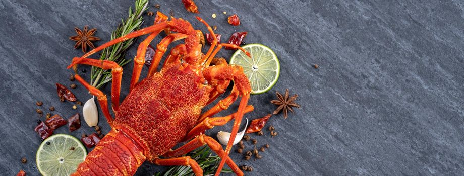 Cooked boiled lobster, delicious dinner seafood meal set with knife and fork on black stone slate background, restaurant menu design, top view, overhead