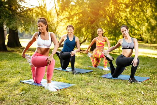 Four beautiful motivated female friends doing stretching exercise in the city park.