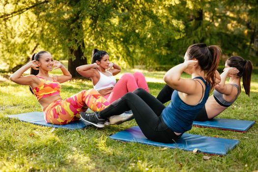 Four beautiful motivated female friends doing sit-up in the city park.