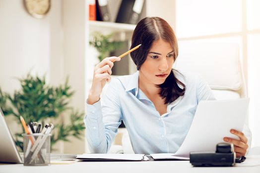 Pensive young woman in the office brainstorming over business report.