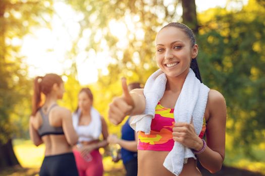 Beautiful sporty happy smiling woman relaxing after doing stretching exercise in the city park. Looking at camera.
