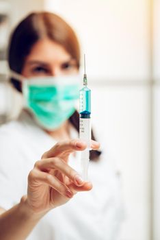 Young female nurse standing in her consulting room and preparing an injection of Anesthesia. Selective focus. Focus on foreground, on injection.