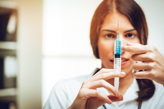 Young female nurse standing in her consulting room and preparing an injection of Anesthesia. Selective focus. Focus on foreground, on injection.