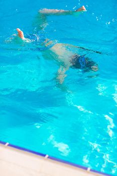 Cute happy little boy in goggles swimming and snorking in the swimming pool. Swimming for kids concept