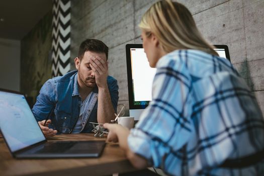 Young handsome frustrated and stressed businessman sitting in the office and complains to his colleague about the pain in his head.