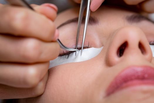 Close-up of a beautician hands applying extended eyelashes to model.  
