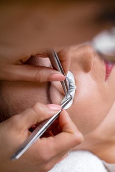 Close-up of a beautician hands applying extended eyelashes to model.  