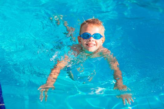 Cute happy little boy in goggles swimming and snorking in the swimming pool. Swimming for kids concept