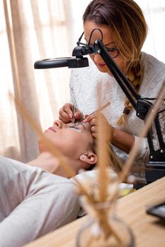 Beautician applying extended eyelashes to model at the beauty salon.