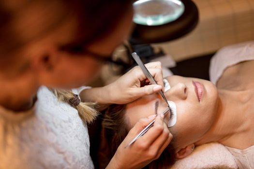 Beautician applying extended eyelashes to model. Top view.