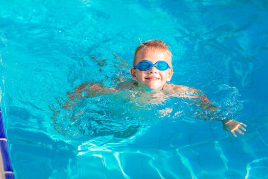 Cute happy little boy in goggles swimming and snorking in the swimming pool. Swimming for kids concept