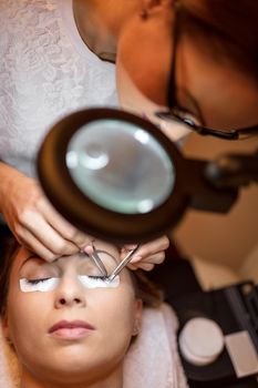 Close-up of beautician applying extended eyelashes to model. Top view. 