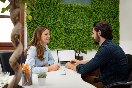 Young successful designers talking about project at the office. Young woman listens her colleague and records the facts in the notebook.