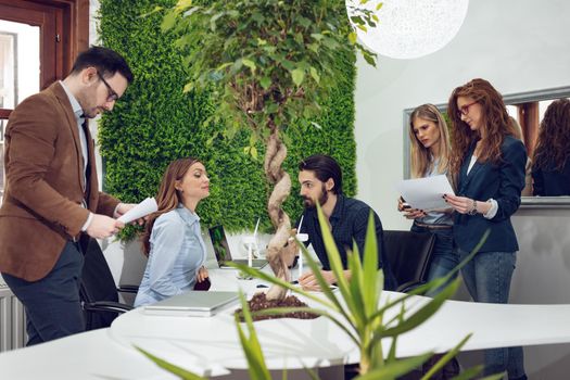 A team of smart qualified skilled young engineers discussing about the project of alternative energy with miniatures of windmill turbines at the table.