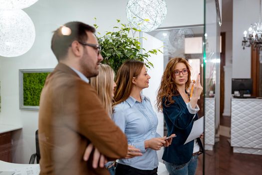 Creative professionals looking over a post it note wall and discussing and female executive standing at the office behind glass wall with sticky notes.