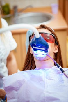 Beautiful young woman in visit at the dentist office, whitening teeth with ultraviolet light. 