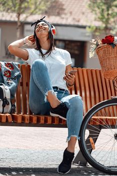 Attractive young woman finds the melody she like best, on the city street, during the stop of riding bike. She is glad of doing this. 