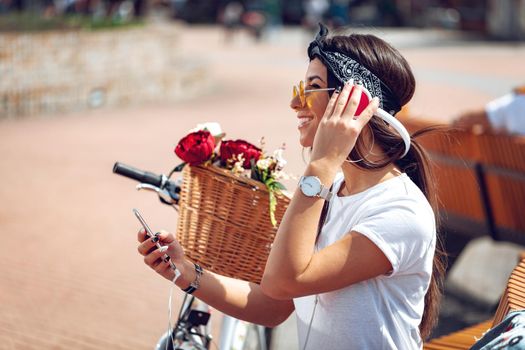 Attractive young woman is trying to find the melody she like best, during the stop of riding bike on the city street. She is glad of doing this. 
