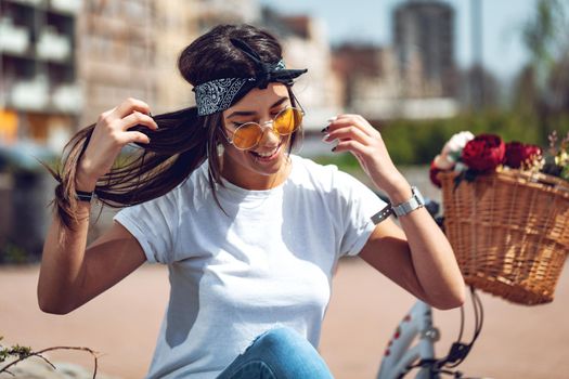 Happy smiling young woman is enjoying in a summer sunny day, beside the bike with flower basket. 