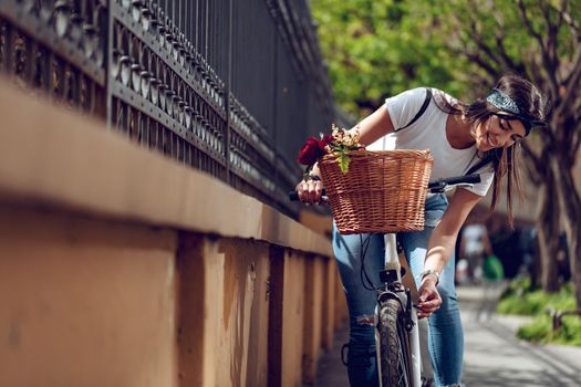 Outdoor shot of young woman ride the bike, along the city road, and checking the wheel of the bike.