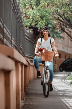 Happy woman riding the bike along the city street, in summer sunny day, smiling of joy during outdoor activity. 