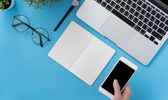 Concept of home office table with fashion accessories, minimal interior with a woman holding smartphone, flat lay, copy space, top view, mockup