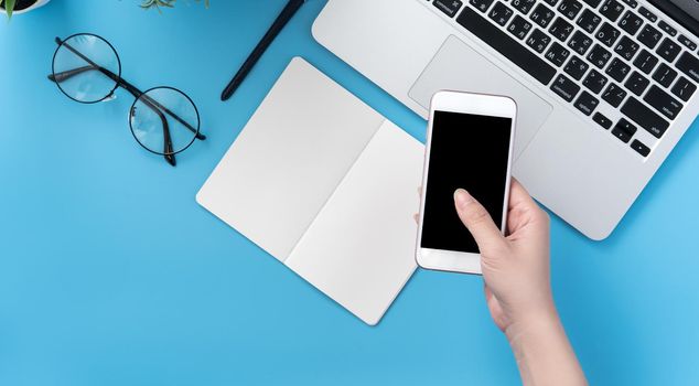Concept of home office table with fashion accessories, minimal interior with a woman holding smartphone, flat lay, copy space, top view, mockup