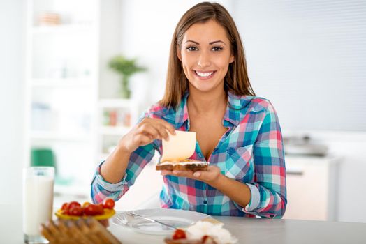 Beautiful young woman preparing healthy sandwich for the breakfast in the domestic kitchen. Looking at camera.