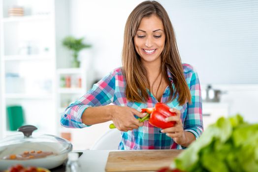 Beautiful young woman making healthy meal in the domestic kitchen. She prepares pepper for filling.