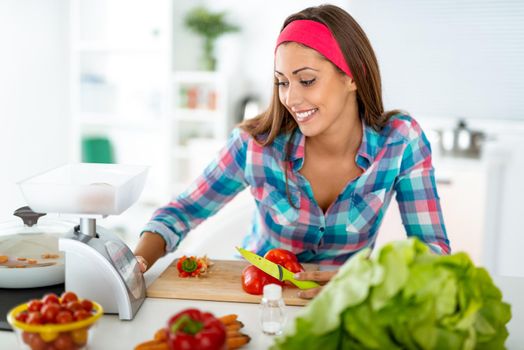 Beautiful young woman making healthy meal in the domestic kitchen. She is weighing something on kitchen scales.