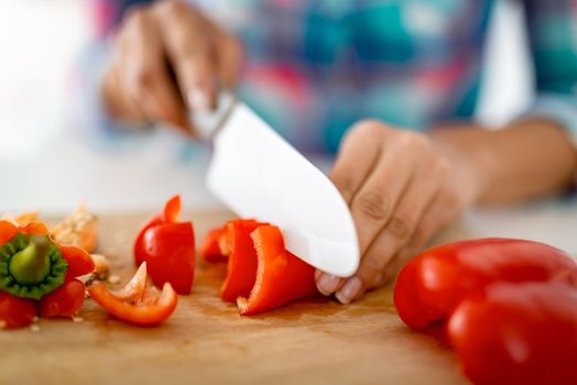 Close-up of a female hands cutting red paprika on the kitchen board.