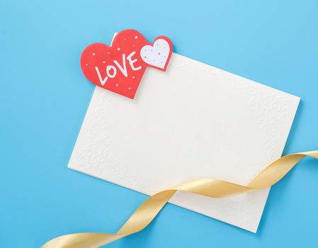 Beautiful greeting card with golden ribbon for Valentine's day, anniversary, mother's day and birthday on blue background, copyspace, topview, mockup, flatlay