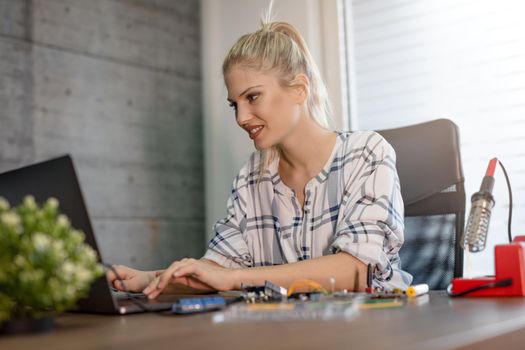 Young woman technician focused on the repair of electronic equipment cecking something on the laptop.