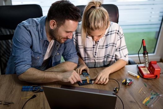 Man helping woman soldering elements of circuit board.  