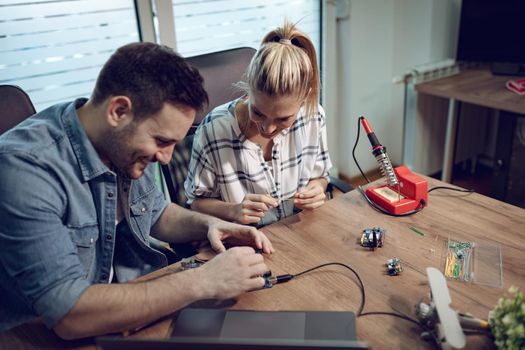 Man helping young woman soldering elements of circuit board.  