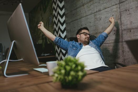 Young handsome overworked businessman sitting in the office stretching and waiting end of working hours. 