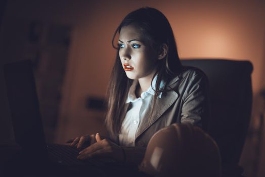 Worried lonely young woman looking at lighted screen of a laptop in night at the home. She is tired because working late.