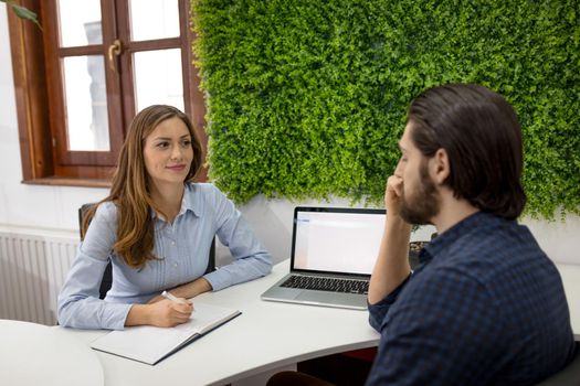 A young man gives an interview for a job, and the data is taken by a young woman.
