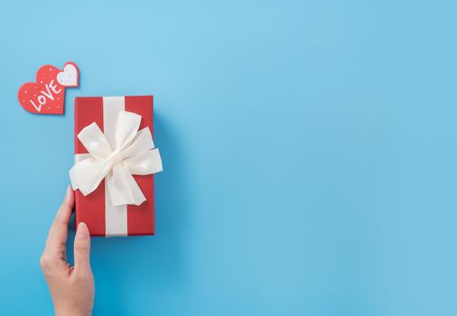 A young woman is giving a gift with greeting on blue background, concept of holiday and celebrate for festival surprising, copyspace, topview