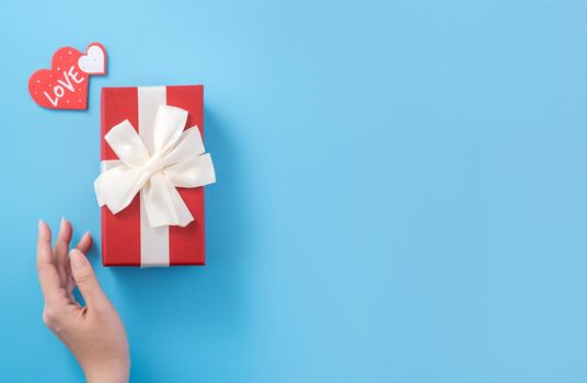 A young woman is giving a gift with greeting on blue background, concept of holiday and celebrate for festival surprising, copyspace, topview