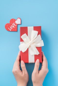 A young woman is giving a gift with greeting on blue background, concept of holiday and celebrate for festival surprising, copyspace, topview