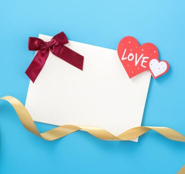 Beautiful greeting card with golden ribbon for Valentine's day, anniversary, mother's day and birthday on blue background, copyspace, topview, mockup, flatlay
