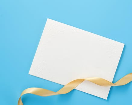 Beautiful greeting card with golden ribbon for Valentine's day, anniversary, mother's day and birthday on blue background, copyspace, topview, mockup, flatlay