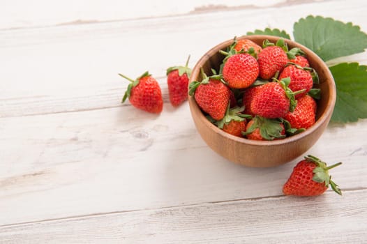A bowl of beautiful and delicious strawberries isolated on a light wooden background, closeup, topview, copyspace.