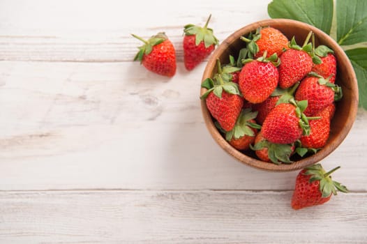 A bowl of beautiful and delicious strawberries isolated on a light wooden background, closeup, topview, copyspace.