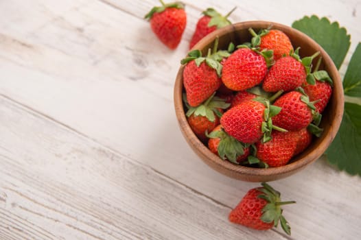 A bowl of beautiful and delicious strawberries isolated on a light wooden background, closeup, topview, copyspace.