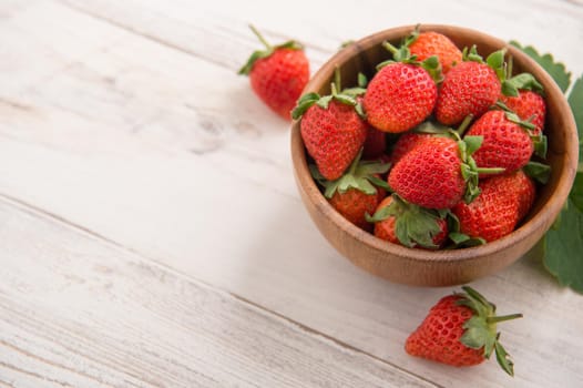 A bowl of beautiful and delicious strawberries isolated on a light wooden background, closeup, topview, copyspace.